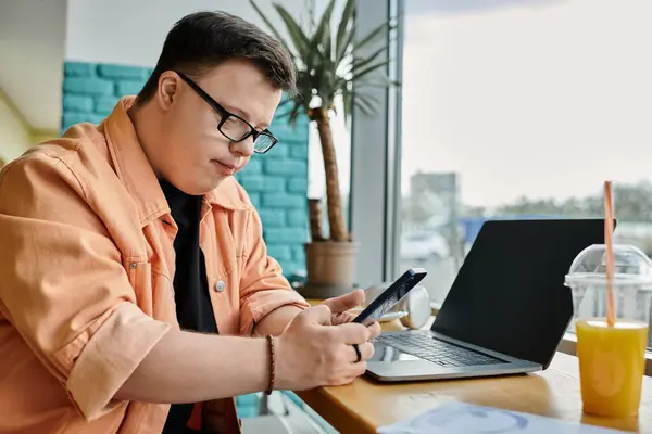 A man with Down syndrome uses his phone and laptop to work in a cafe. — Stock Photo