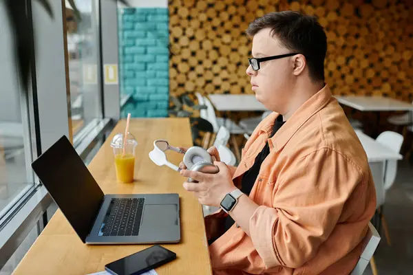 A man with Down syndrome works on his laptop in a cafe, taking a break to adjust his headphones. — Stock Photo