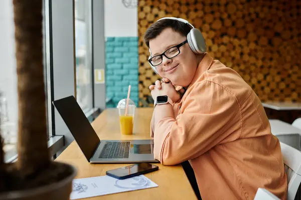 A man with down syndrome works remotely on a laptop in a cafe, wearing headphones and smiling. — Stock Photo