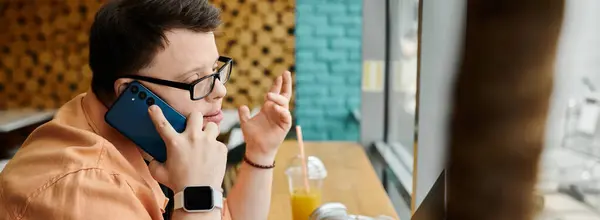 A young man with down syndrome works on his laptop in a cafe, talking on the phone. — Stock Photo