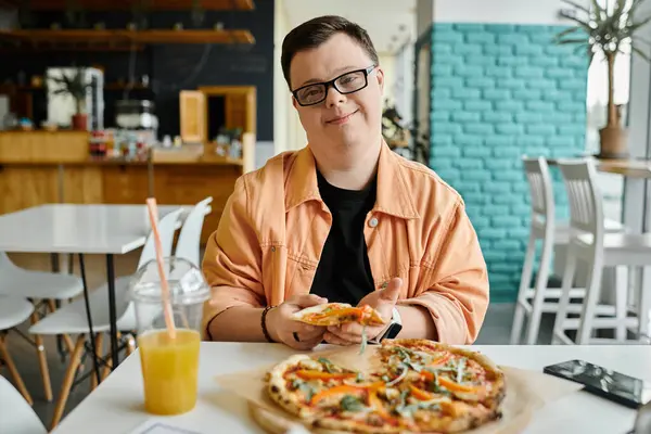 A man with Down syndrome smiles as he takes a bite of a delicious pizza in a cafe setting. — Stock Photo
