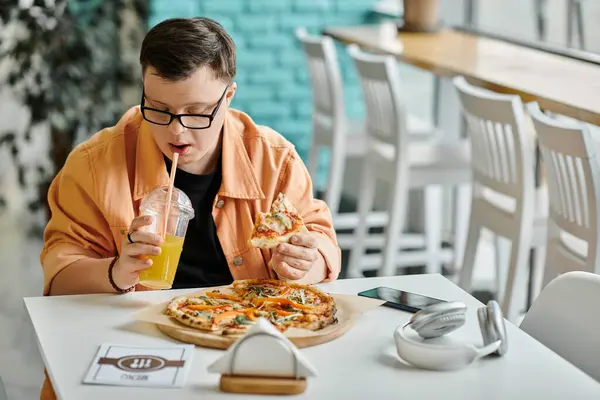 A man with Down syndrome savors a slice of pizza while enjoying a beverage at a cafe. — Stock Photo