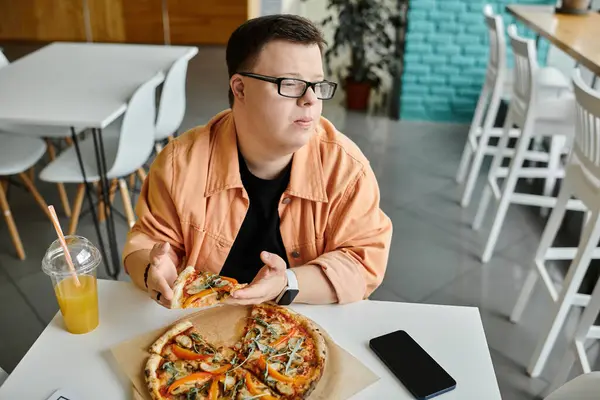 Man in glasses with down syndrome eating pizza next to his smartphone in cafe — Stock Photo