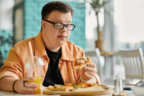 A man with Down Syndrome sits in a cafe, enjoying a slice of pizza with a refreshing drink. — Stock Photo