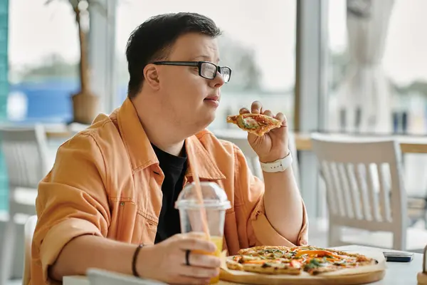 Ein Mann mit Down-Syndrom sitzt an einem Cafétisch und beißt in ein leckeres Pizzastück. — Stockfoto