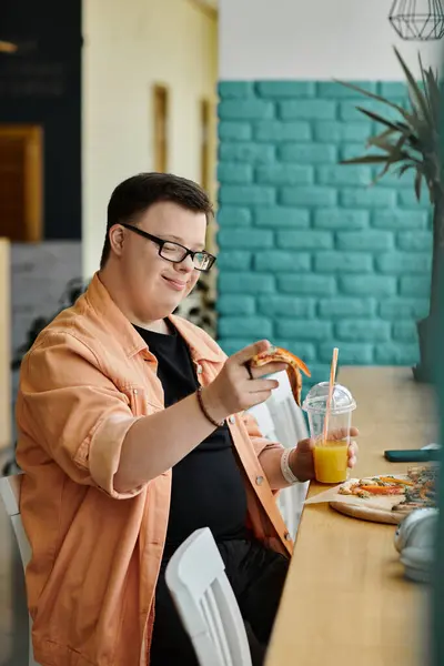 A man with Down syndrome smiles as he eats a slice of pizza in a cafe. — Stock Photo