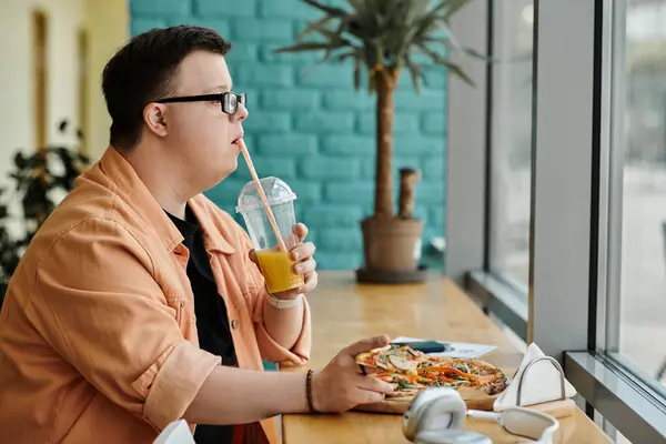 A man with Down syndrome sits at a cafe table, enjoying a slice of pizza and a refreshing drink. — Stock Photo
