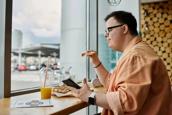 A man with Down syndrome enjoys a delicious pizza while browsing on his phone at a cafe. — Stock Photo