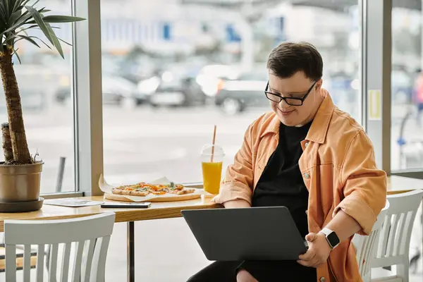 A man with Down syndrome smiles while using a laptop at a cafe table with a slice of pizza. — Stock Photo