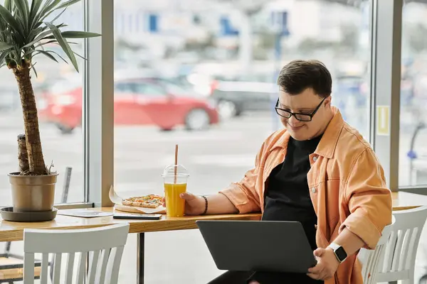 A man with Down syndrome smiles as he eats pizza and uses a laptop in a cafe. — Stock Photo
