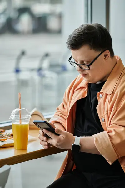 A man wearing glasses and a peach-colored jacket checks his phone while enjoying a beverage in a cafe. — Stock Photo