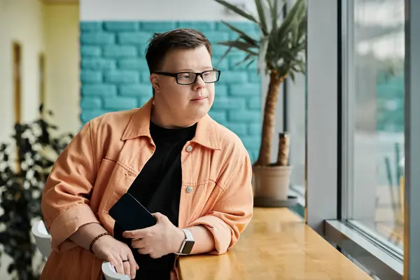 A man with Down Syndrome sits by the window in a cafe, enjoying a moment of peace and reflection. — Stock Photo