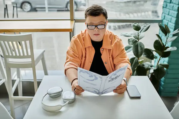 A man with Down syndrome sits at a cafe table, thoughtfully studying the menu before making his meal choice. — Stock Photo