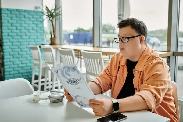 A man with Down syndrome sits at a cafe table, thoughtfully reviewing the menu. — Stock Photo