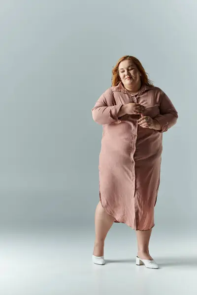 A woman in a long pink dress stands with her arms crossed, smiling in a studio. — Stock Photo