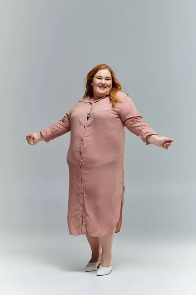 A smiling woman with red hair poses in a flowing, long-sleeved dress. — Stock Photo
