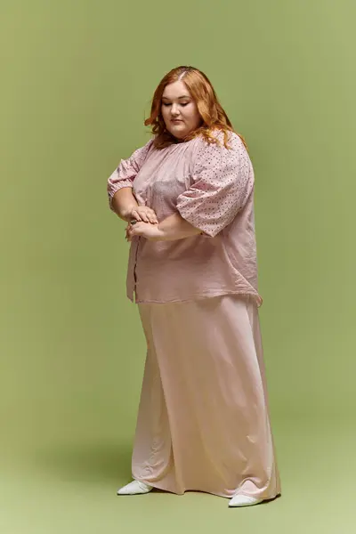 A woman in a pink blouse and skirt poses against a green background. — Stock Photo