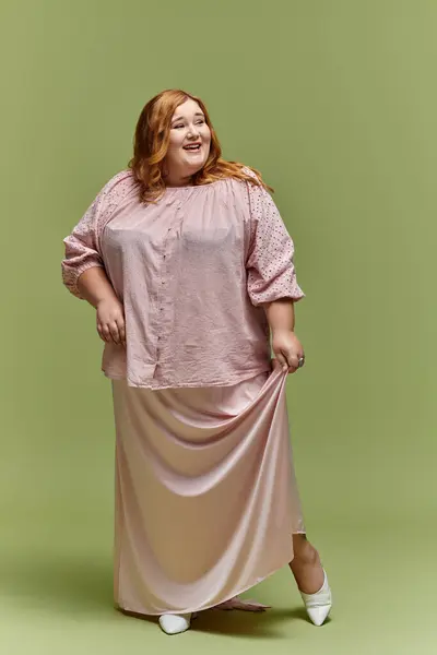 A woman in a pink blouse and skirt smiles and poses against a green backdrop. — Stock Photo
