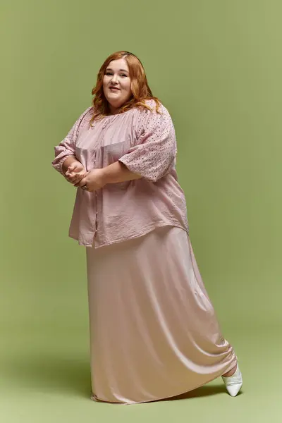 A plus size woman in blush stands confidently on a green backdrop, her smile captivating — Stock Photo