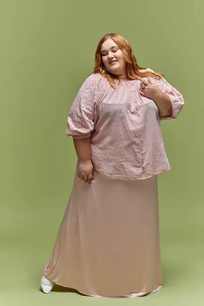 A woman in a flowing pink blouse and skirt poses against a green background. — Stock Photo