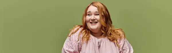 A plus-size woman with red hair laughs joyfully in front of a green background. — Stock Photo