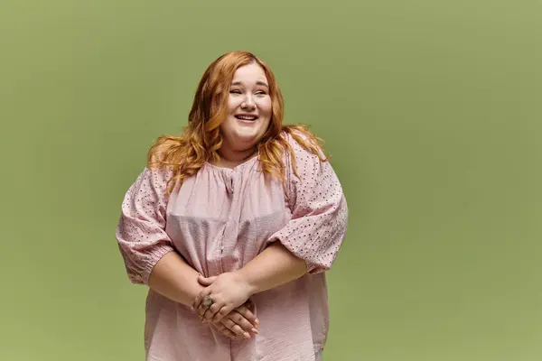 Una mujer con el pelo largo y rojo se ríe mientras está de pie sobre un fondo verde claro. - foto de stock