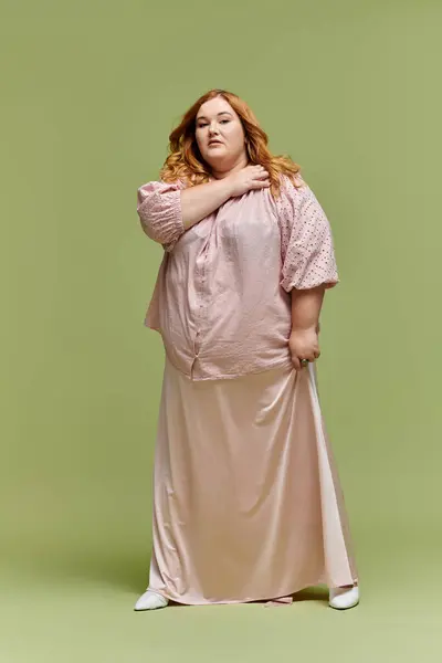 A woman in a pink blouse and skirt poses against a green background. — Stock Photo