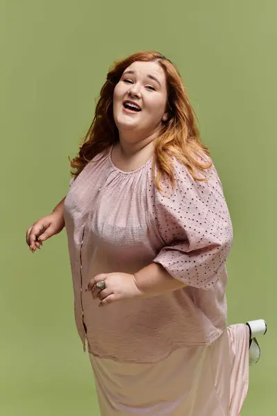 A plus-size woman in a light pink dress smiles and poses in front of a green background. — Stock Photo