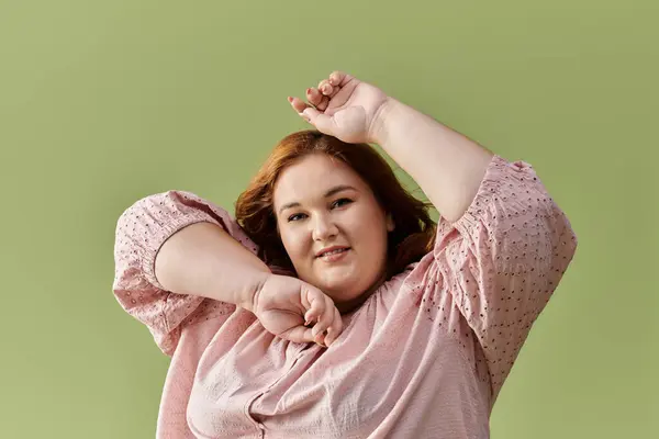 Женщина plus-size в розовой блузке ярко улыбается на фоне зеленого задника. — стоковое фото