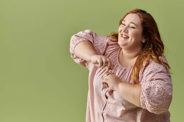 A woman smiles brightly in a pink blouse against a green background. — Stock Photo