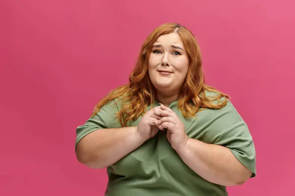 A woman with red hair, wearing a green t-shirt, smiles and poses against a pink background. — Stock Photo