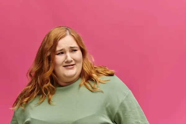 Uma mulher com cabelo vermelho longo olha pensativamente fora da câmera, seu rosto emoldurado por uma parede rosa vibrante. — Fotografia de Stock