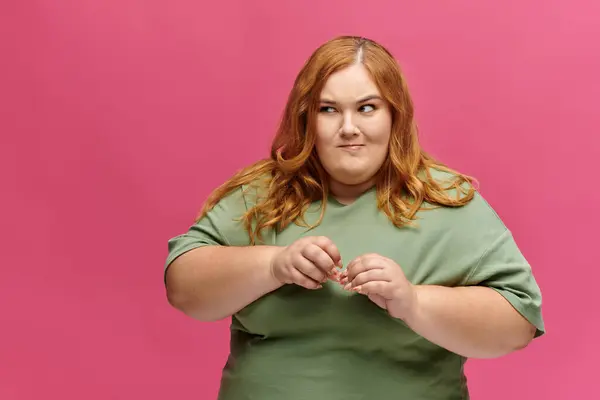 A plus size woman with red hair poses playfully against a pink background. — Stock Photo