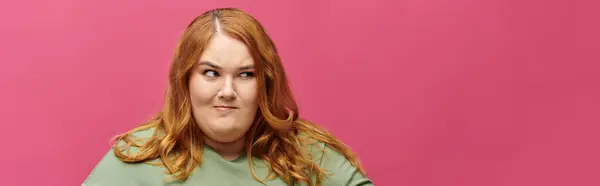 A woman with long red hair, wearing a green shirt, looks thoughtfully off-screen. — Stock Photo