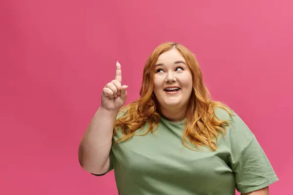Una mujer de talla grande con una camisa verde apunta hacia arriba con una expresión reflexiva en su cara. - foto de stock