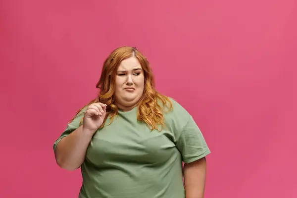 Una mujer de talla grande con una camisa verde mira hacia otro lado con una expresión escéptica. - foto de stock