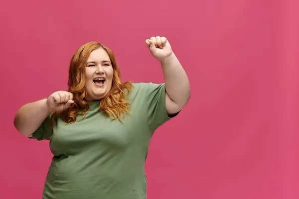 A plus size woman dances enthusiastically in front of a pink backdrop. — Stock Photo