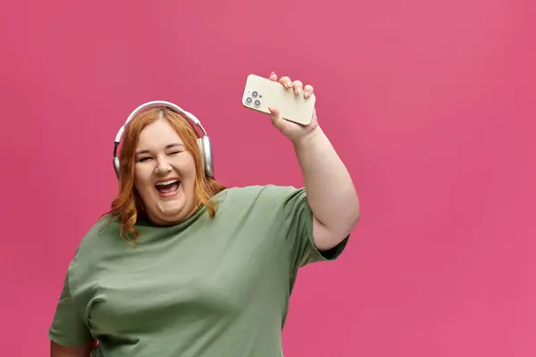 Женщина plus-size с наушниками счастливо сидит, держа в руках телефон. — стоковое фото