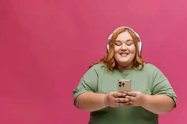 Uma mulher em fones de ouvido sorri enquanto olha para o telefone. — Fotografia de Stock