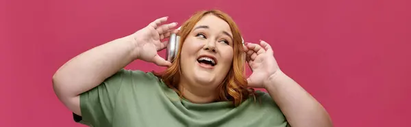 Una donna con i capelli rossi e una camicia verde canta insieme alla musica mentre indossa le cuffie. — Foto stock