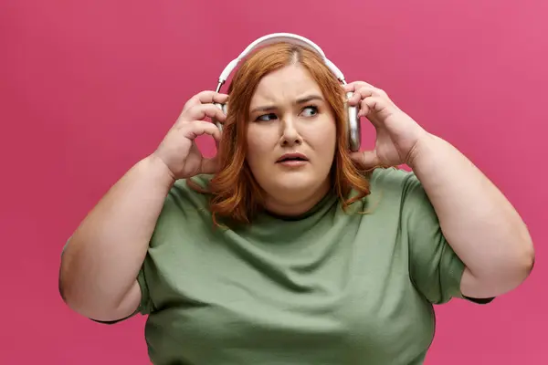 Una donna che indossa le cuffie li regola su uno sfondo rosa. — Foto stock