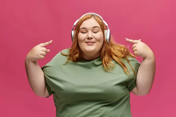 Uma mulher com cabelos vermelhos e fones de ouvido sorri enquanto ouve música. — Fotografia de Stock