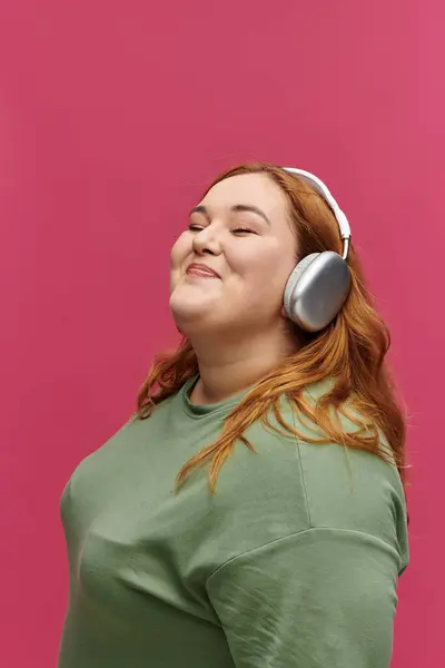 Una mujer con una camisa verde, con los ojos cerrados, sonríe mientras escucha música a través de auriculares. - foto de stock