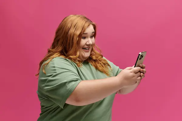 A woman smiles brightly as she looks at her phone, holding it in both hands. — Stock Photo