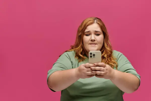 A woman in a green shirt looks thoughtfully at her phone, her expression hinting at contemplation. — Stock Photo