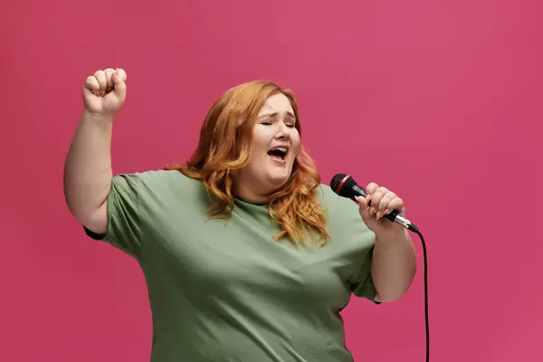 Plus size woman with long red hair sings into a raised arm carrying a microphone — Stock Photo