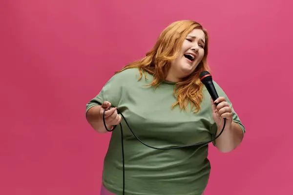 Joyful, plus-size woman in green shirt sings passionately into a microphone — Stock Photo