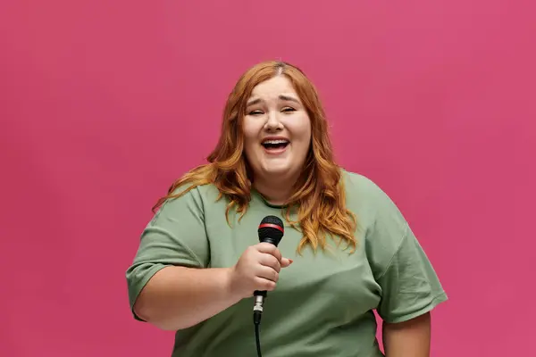 Eine Plus-Size-Frau mit roten Haaren singt in ein Mikrofon und lächelt strahlend. — Stockfoto