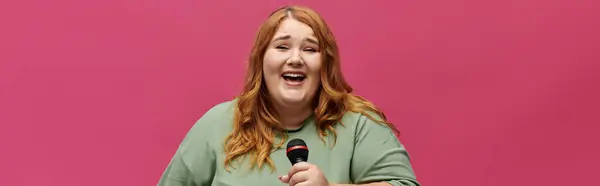 A woman with long red hair sings into a microphone in front of a pink background. — Stock Photo