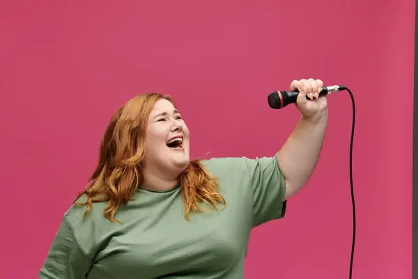 Una donna con lunghi capelli rossi canta in un microfono davanti a uno sfondo rosa. — Foto stock
